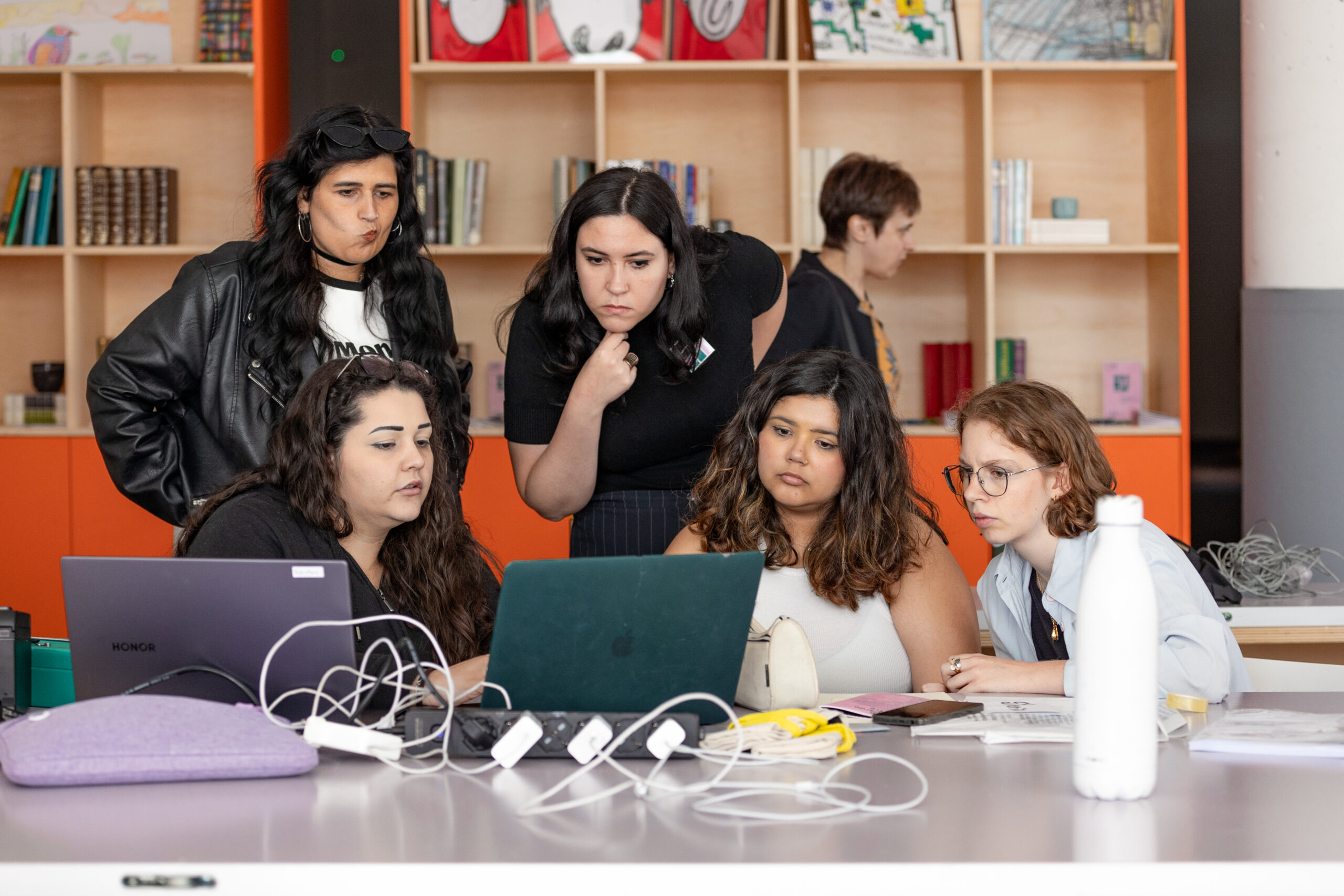 Quattro ragazze della Direzione Artistica Partecipata Under 30 osservano qualcosa sul pc di una persona dello staff.