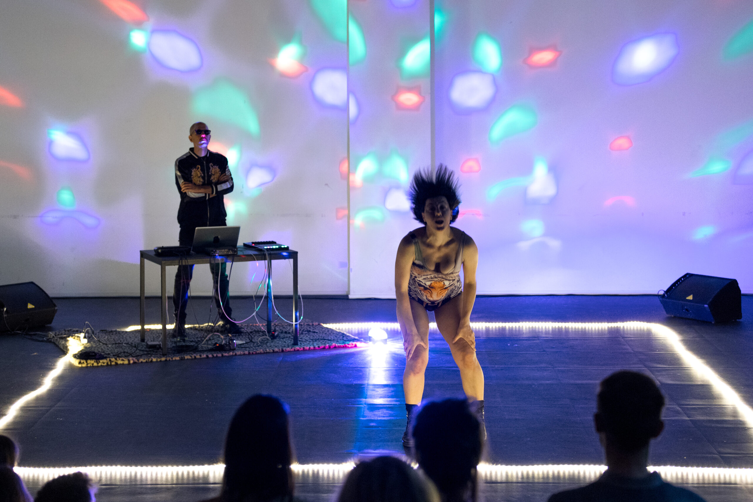 La performer di “Wannabe” balla circondata da luci colorate da discoteca. Sull’angolo in fondo a sinistra il DJ.