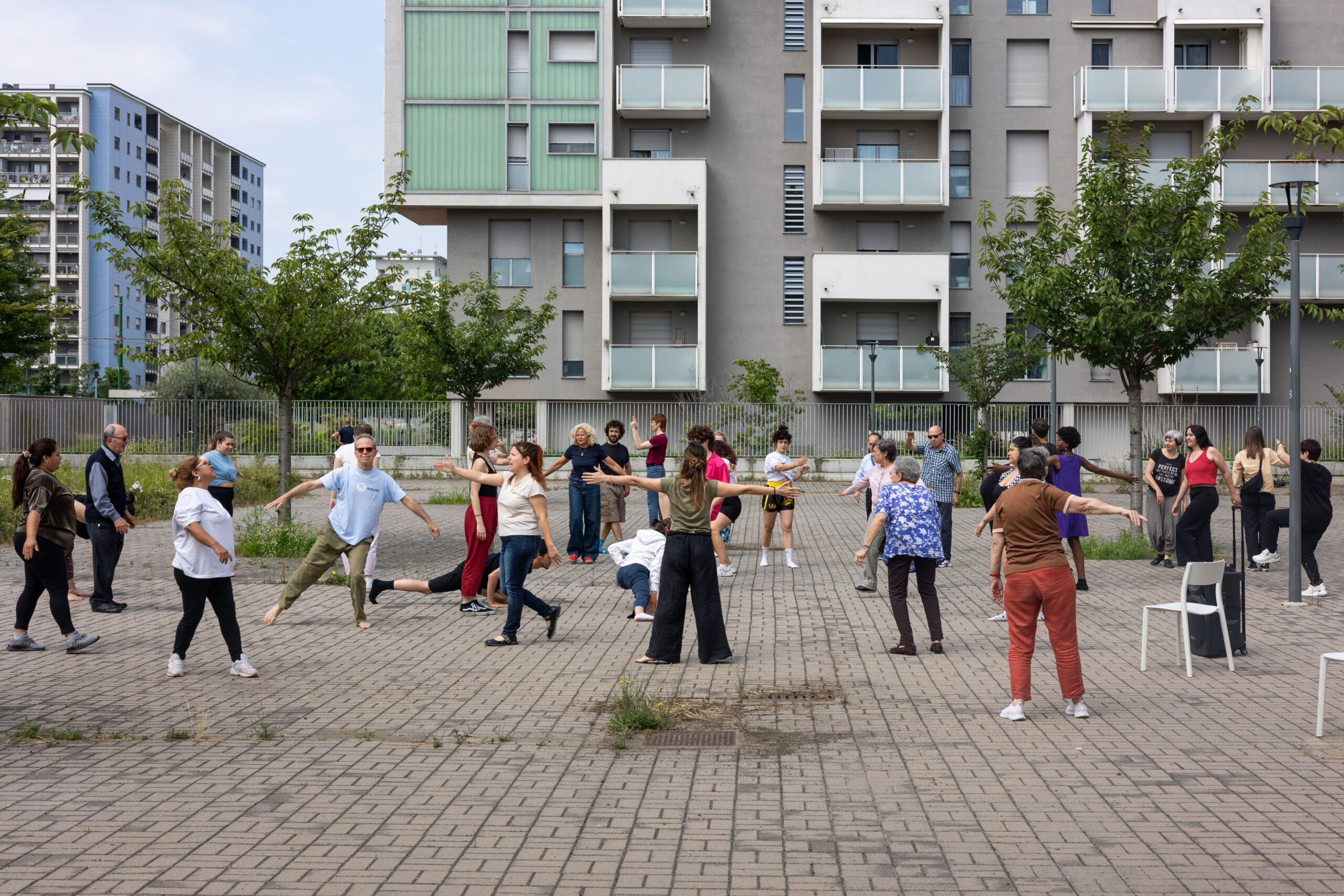 Un nutrito gruppo intergenerazionale si muove nello spazio pubblico all’aperto durante il laboratorio “Dance Well”.