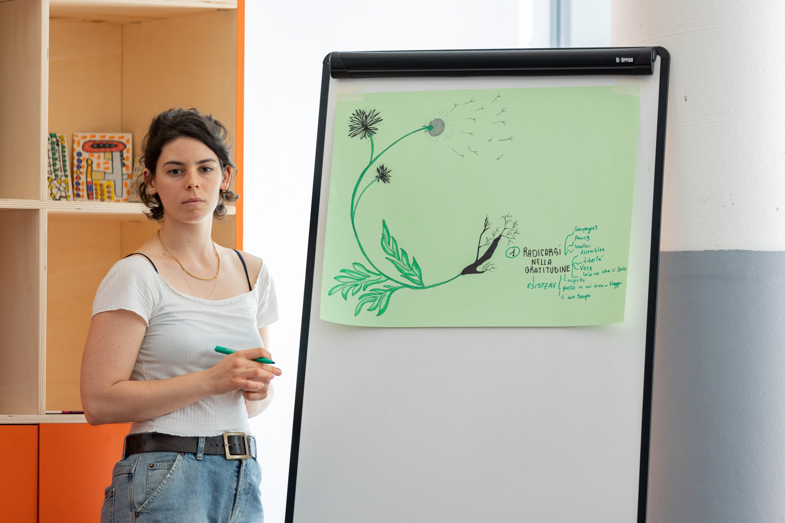 Una relatrice dai capelli corti vicino a una lavagna su cui è disegnato un fiore durante il laboratorio “Esercizi di immaginazione collettiva”.