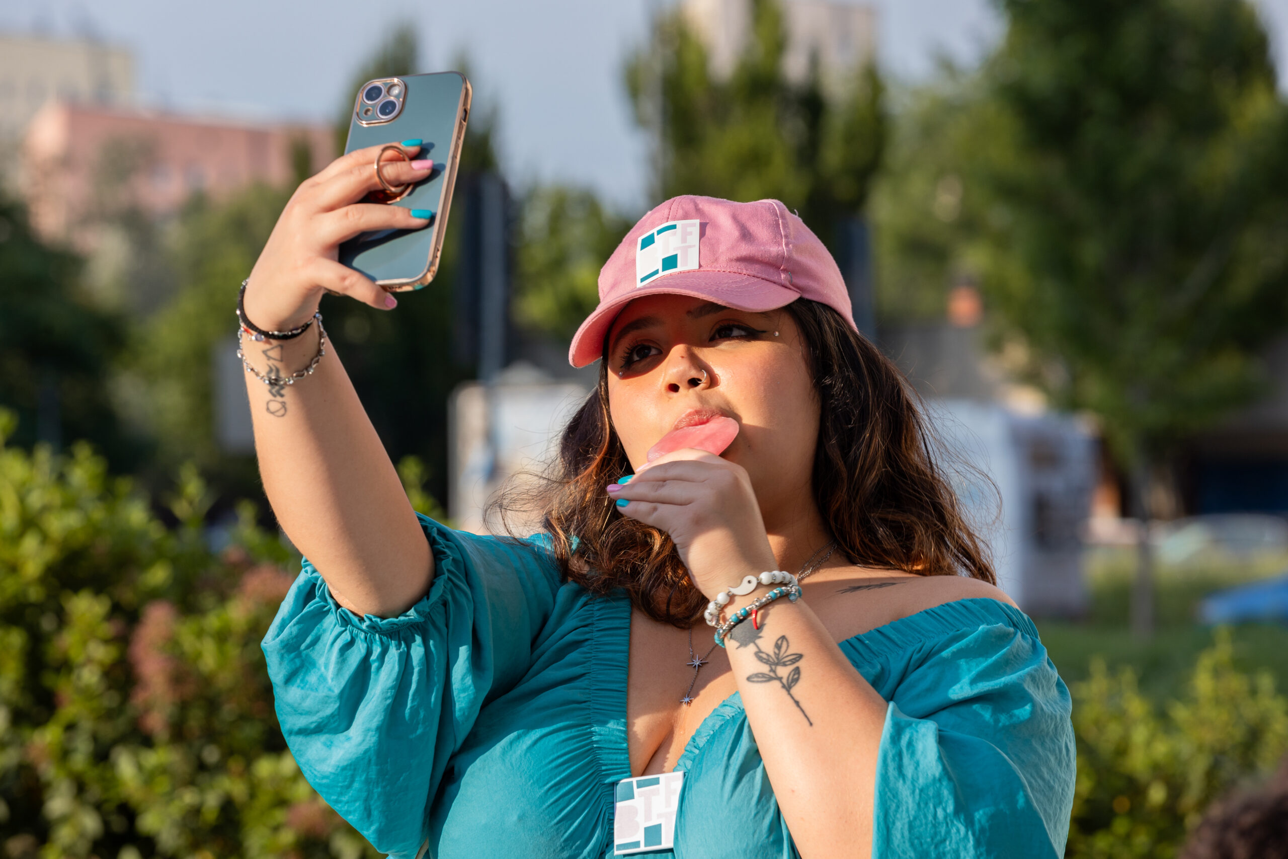 Una ragazza della Direzione Artistica Partecipata Under 30, che indossa i colori del festival, si fa un selfie con il cellulare mentre mangia un ghiacciolo.