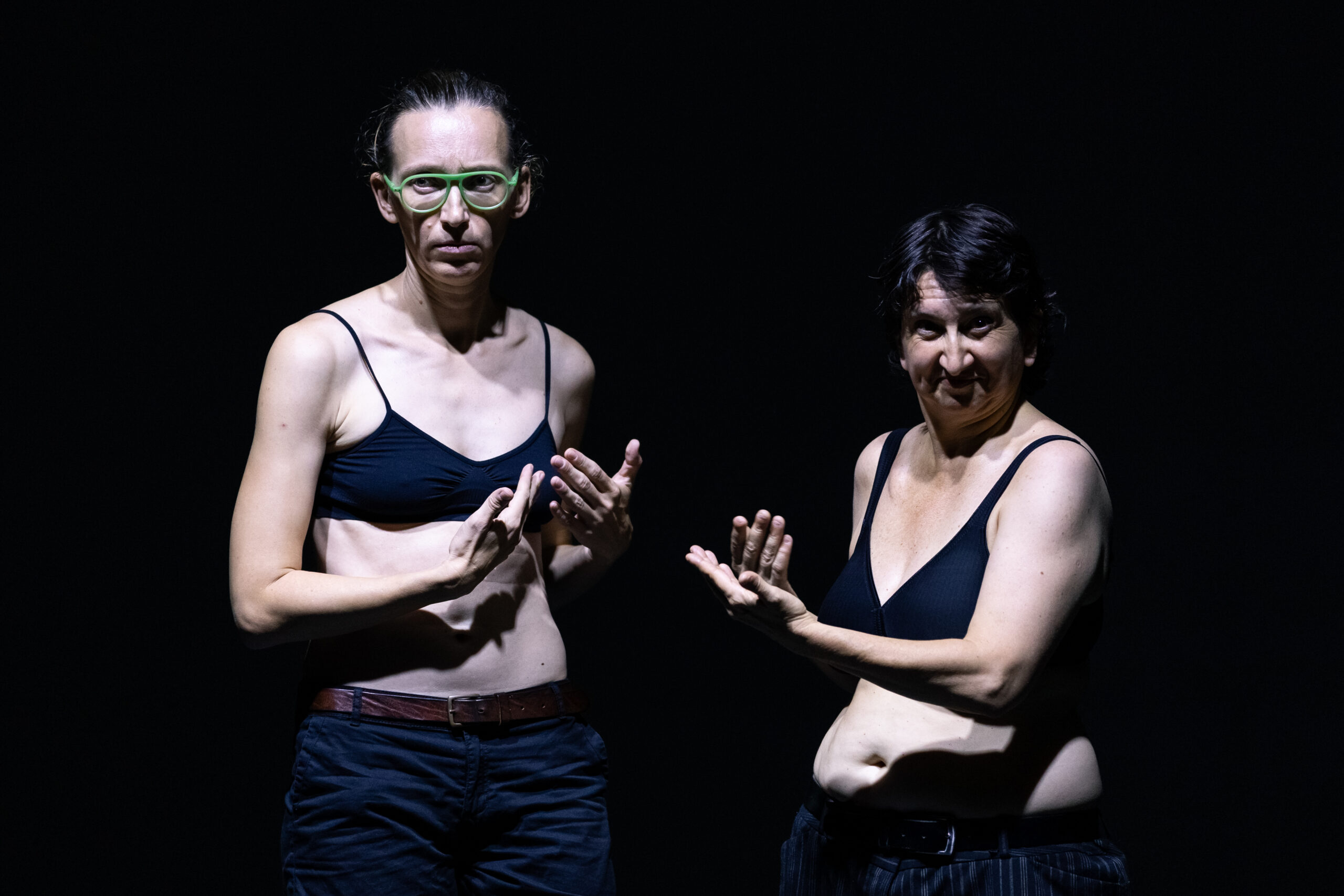 Le due performer di “Insectum” in Quartiere Adriano, con fisicità molto diverse, in reggiseno e jeans gesticolano su sfondo scuro.