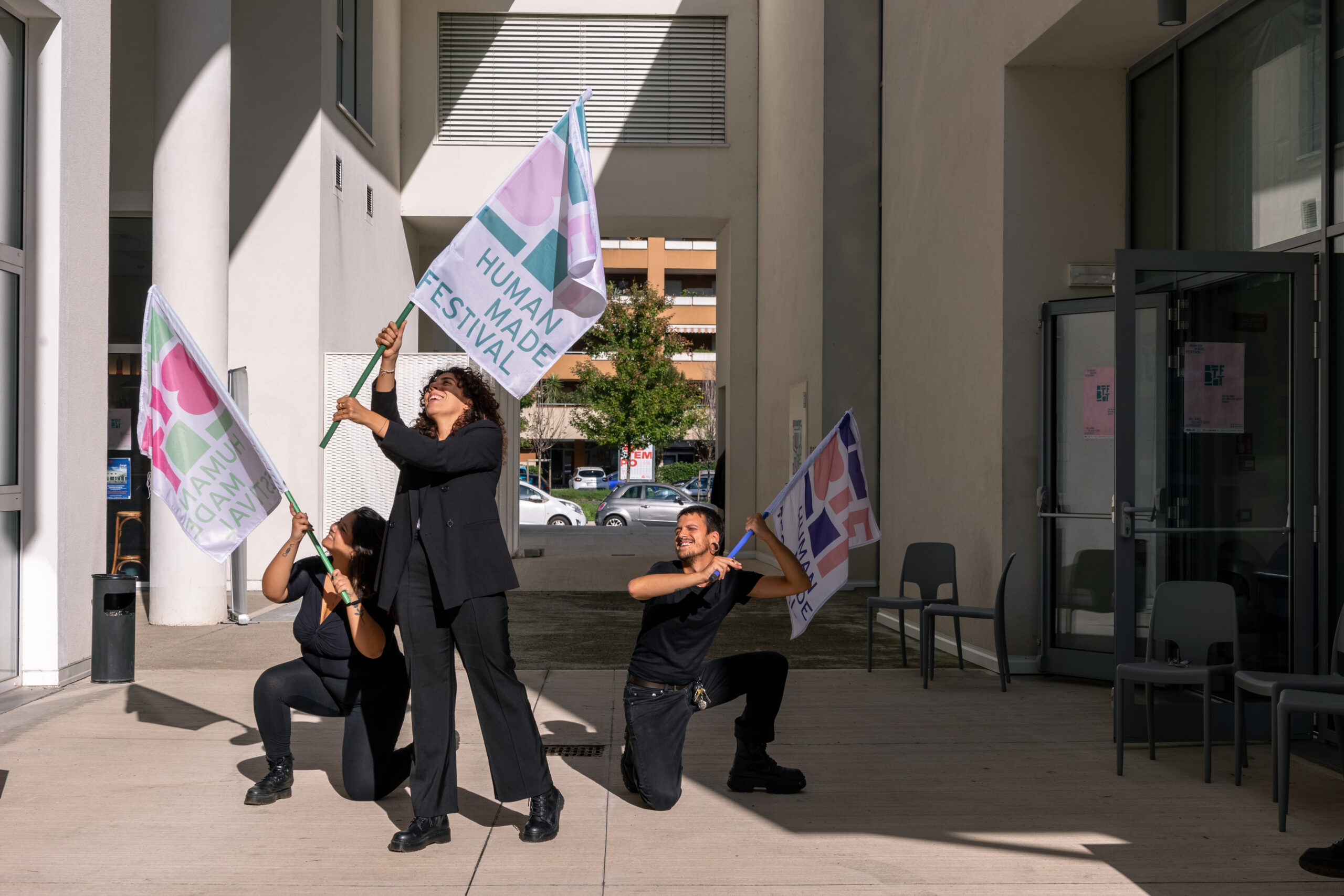 Tre giovani della Direzione Artistica Partecipata Under 30 di BTTF sventolano le bandiere del festival di fronte all’ingresso dello spazio.