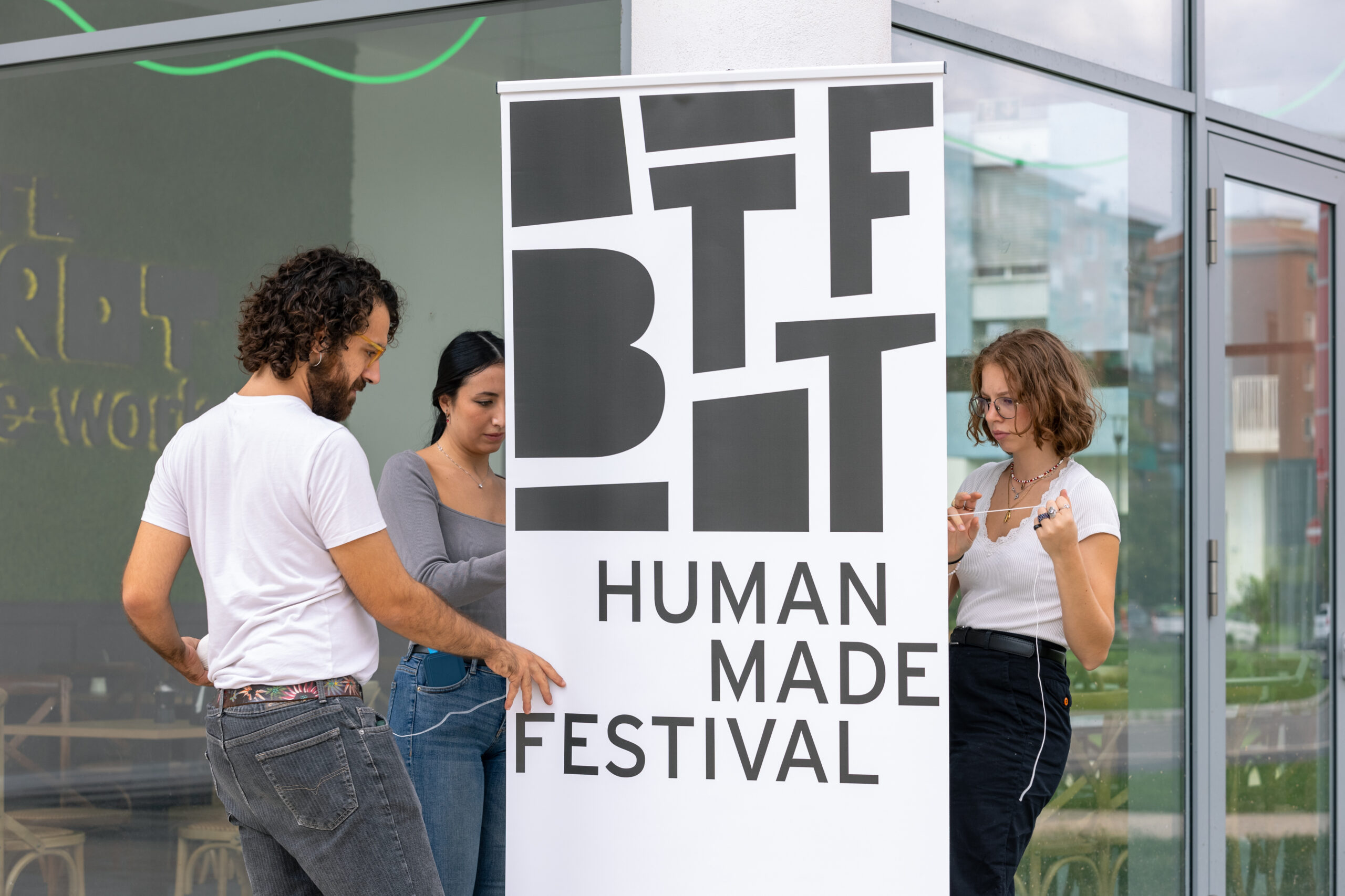 Un ragazzo e due ragazze della Direzione Artistica Partecipata Under 30 allestiscono un roll up con il logo di BTTF e il claim Human Made Festival.