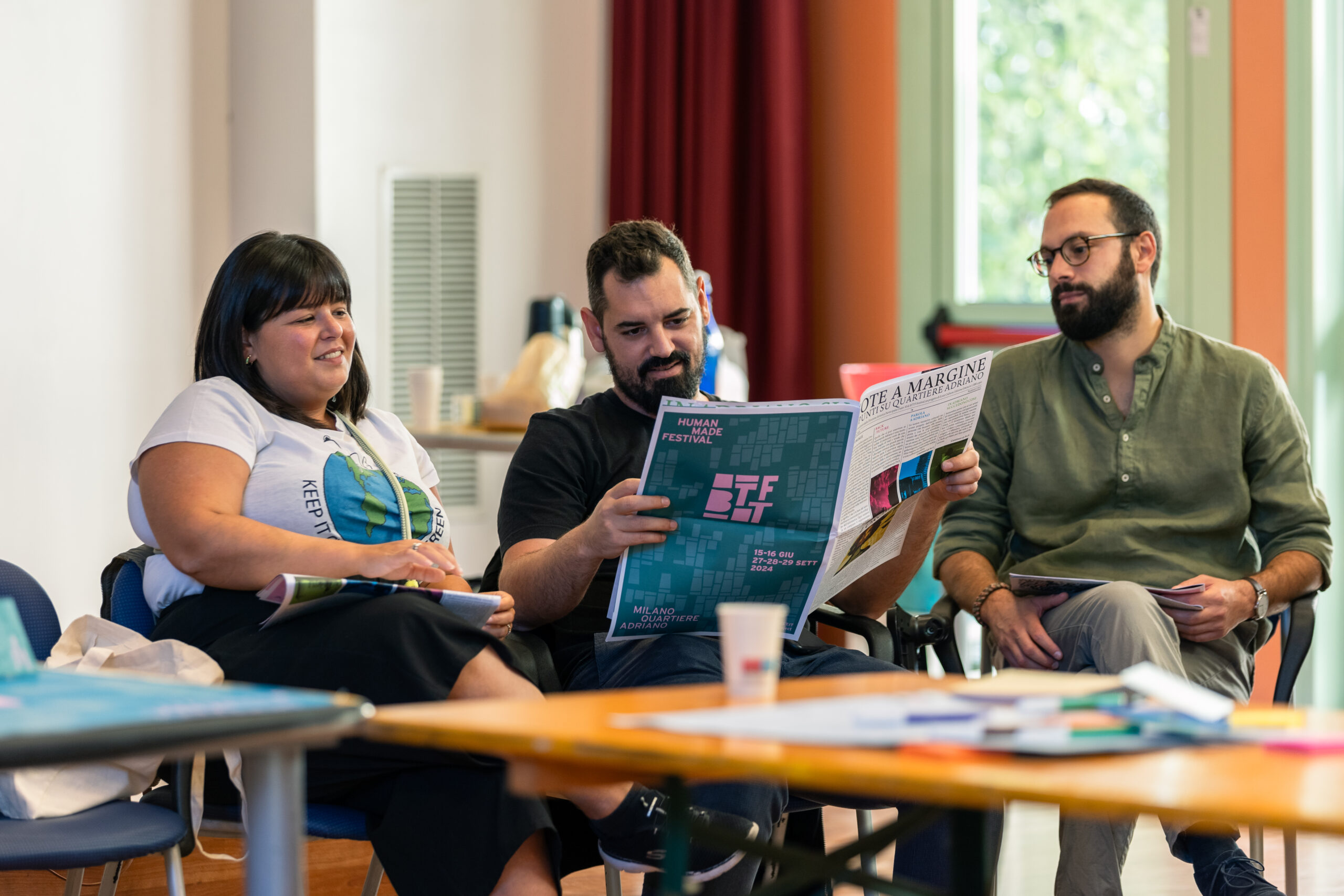 Una relatrice e due ragazzi del pubblico leggono insieme una copia del giornale “Note a margine” durante una pausa del convegno “InVisible”.
