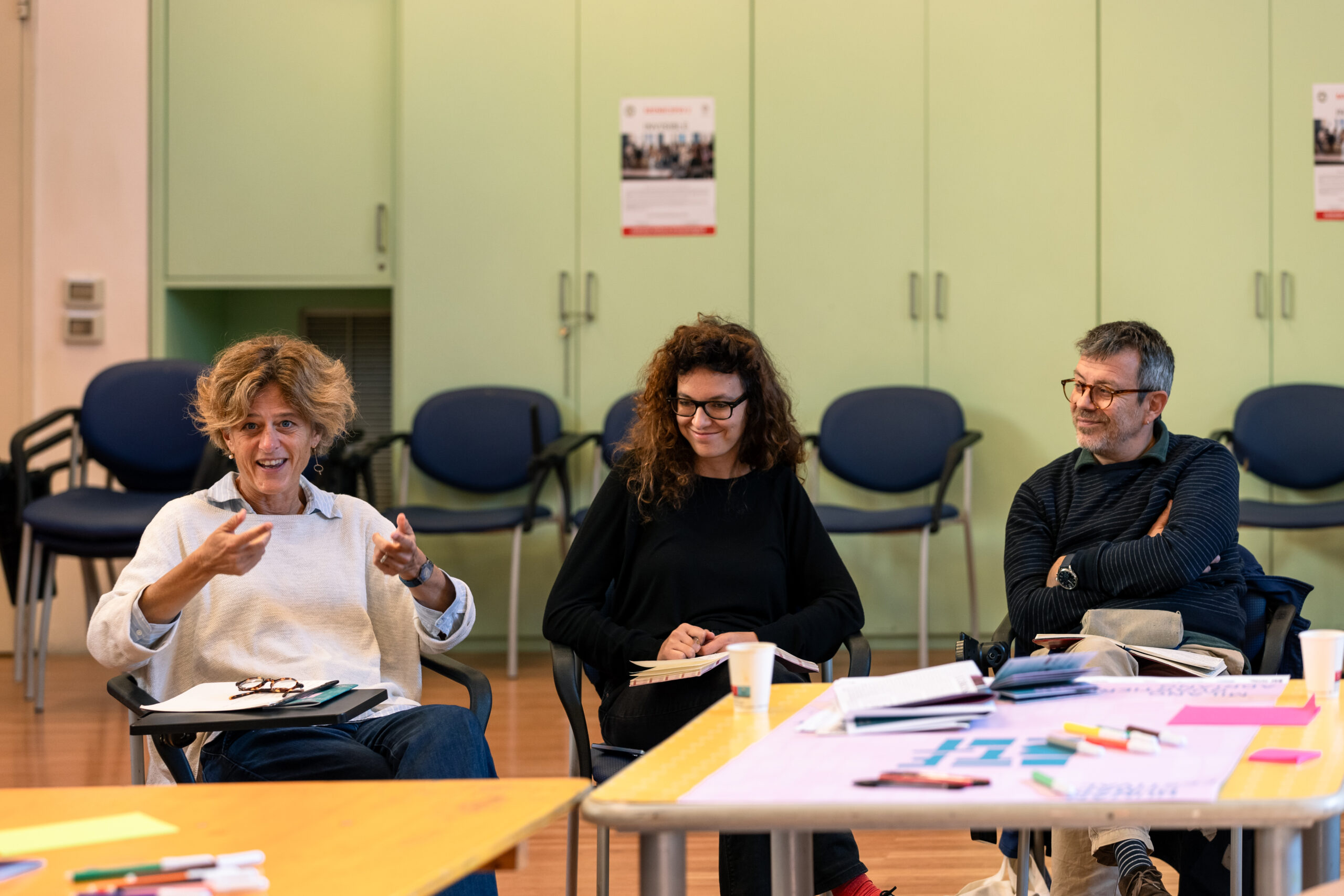 Due relatrici e un relatore del convegno “InVisible”, seduti in uno spazio informale, sorridono e gesticolano parlando alle persone presenti.