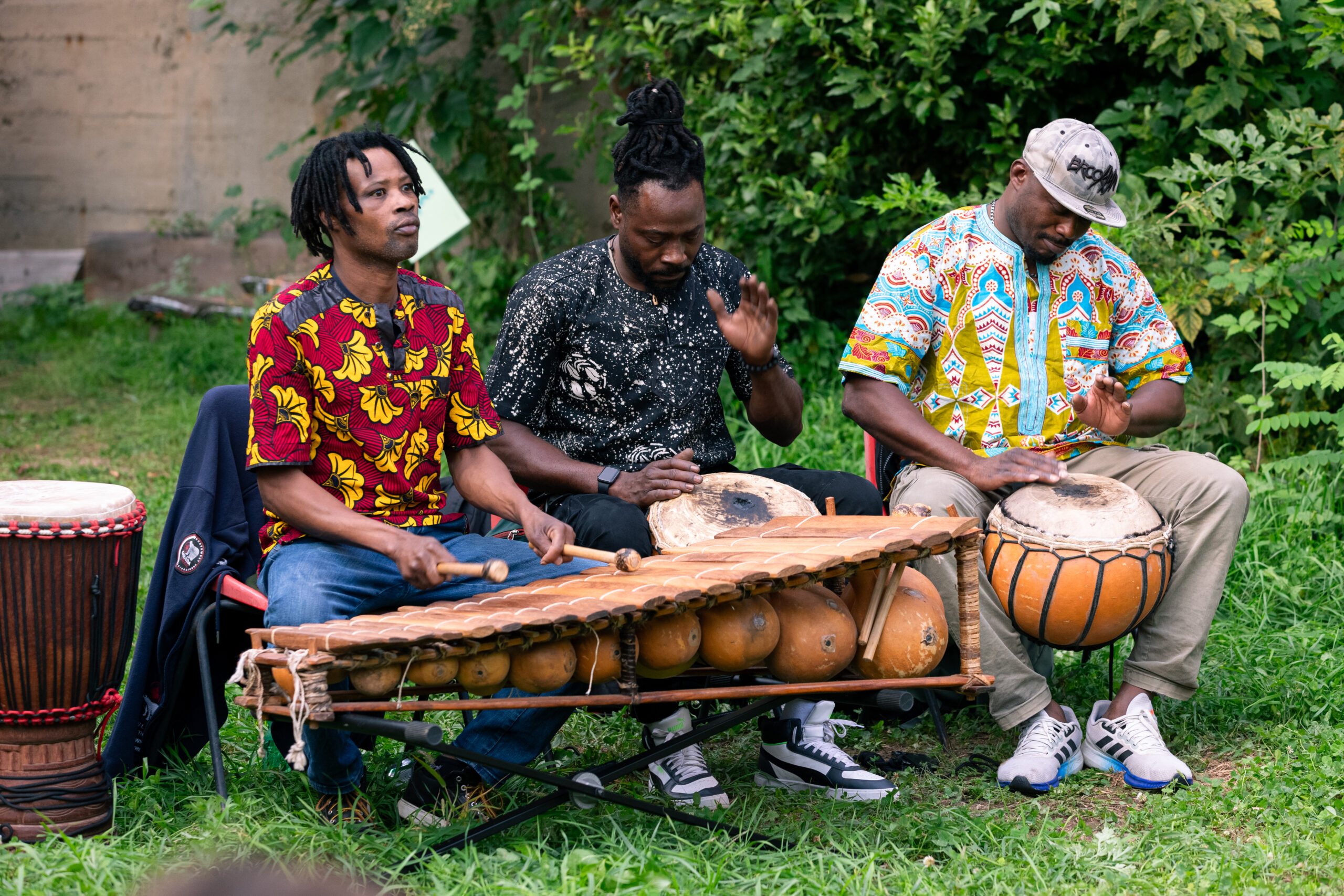 Tre musicisti africani suonano percussioni e strumenti tradizionali durante la performance “Yele” in un giardino cittadino.
